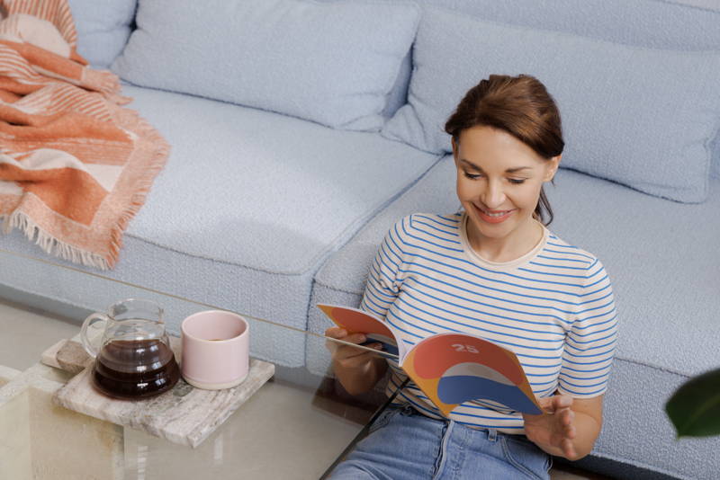 Woman reading a book leaning against the couch with a cup in her hand, a Hario V60 Range Server on the table