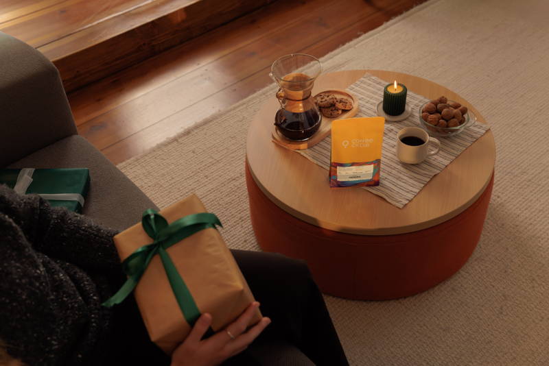 Frau hält Geschenk, auf dem Tisch steht eine Chemex, Hendra Filterkaffee, Kekse, eine Tasse und eine Kerze