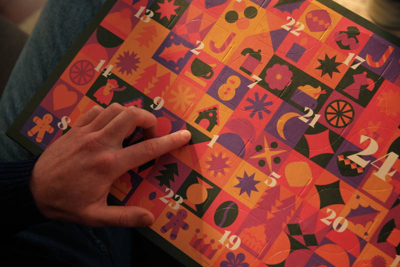 Eine Person zeigt auf das erste Türchen eines Adventskalenders.