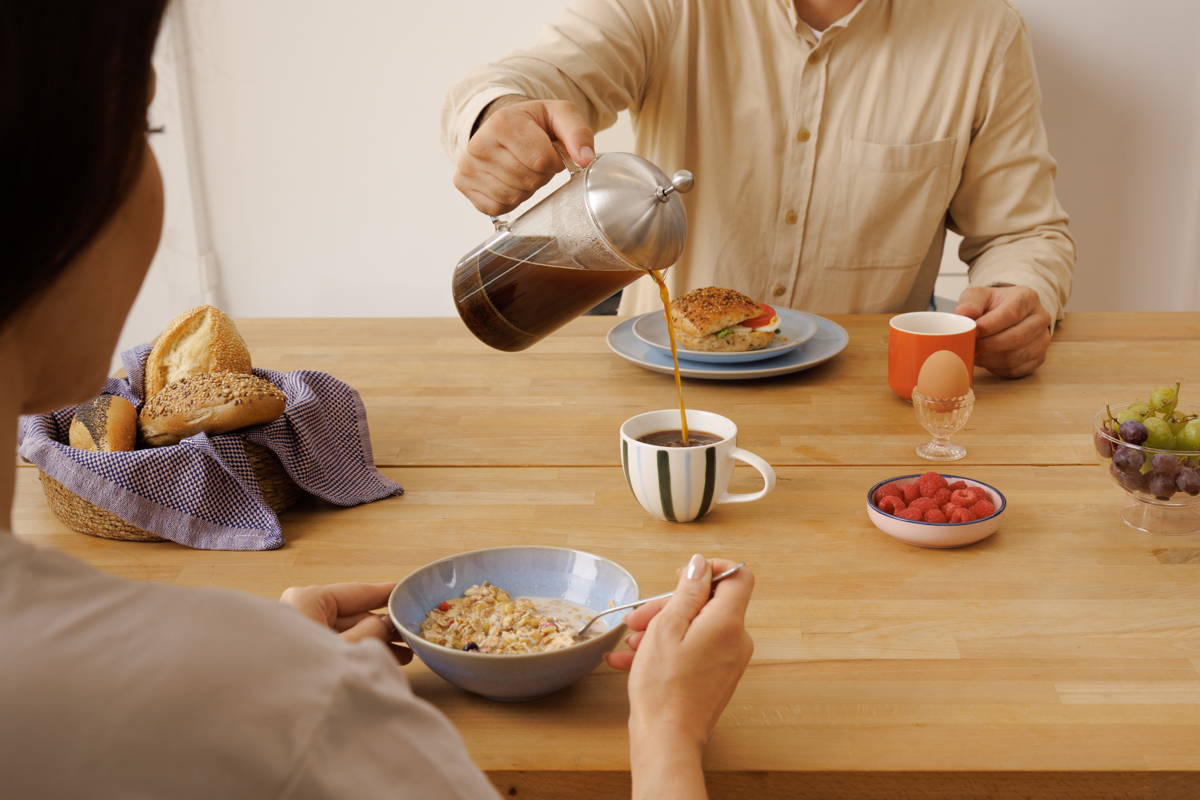 Mann schenkt Frau am Frühstückstisch Kaffee aus einer French Press in die Tasse