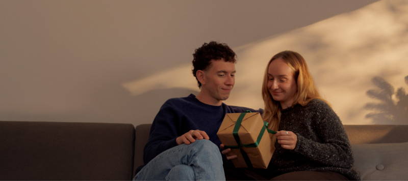 Mann und Frau packen auf der Couch ein Geschenk aus