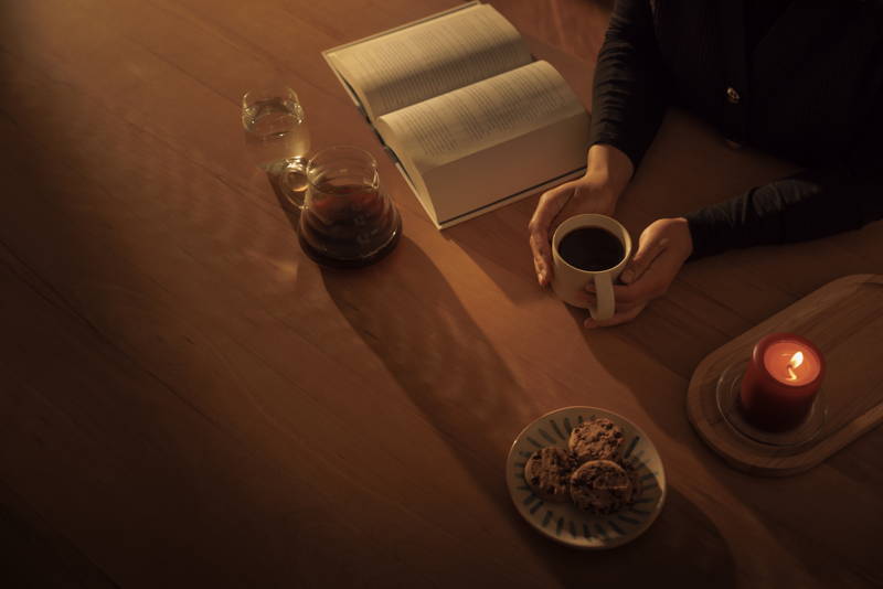 Eine Person sitzt am Esstisch, liest und trinkt Kaffee