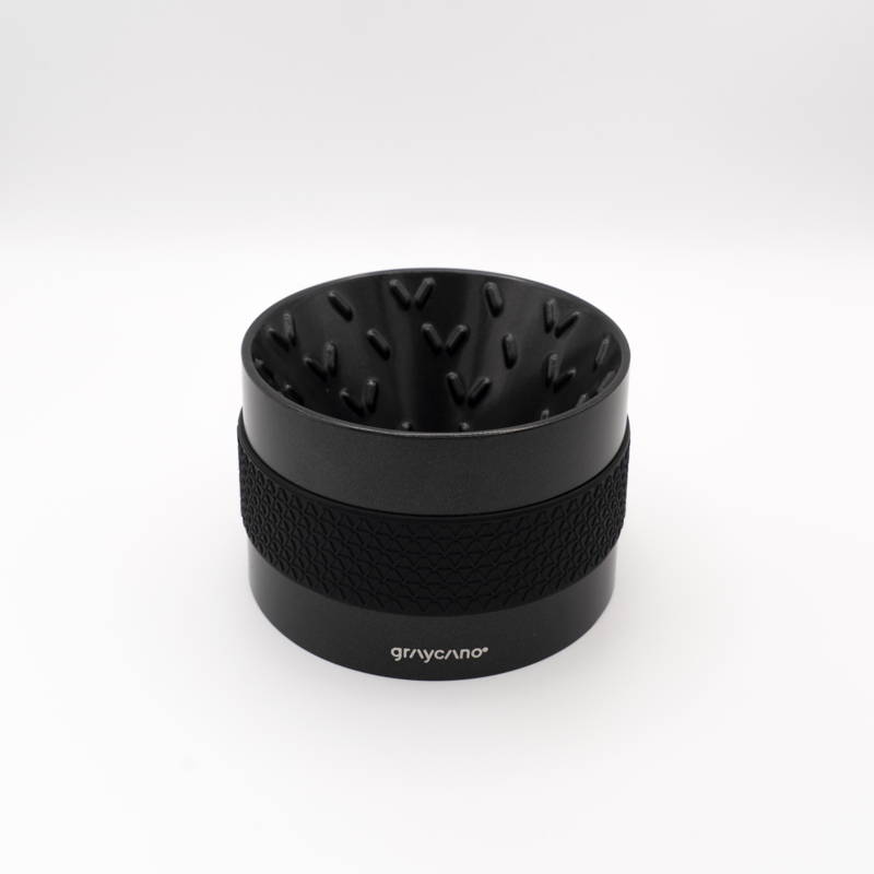 A matte black graycano coffee dripper against a white background. The cylindrical dripper features distinctive V-shaped protrusions on the inside wall and a textured black silicone sleeve wrapped around the outside. The brand name "graycano" is printed near the bottom edge.
