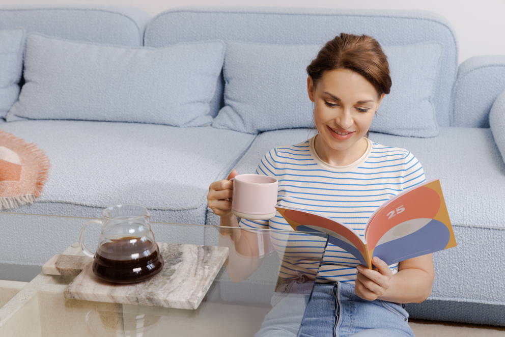 Frau liest ein Buch an die Couch gelehnt mit einer Tasse in der Hand, auf dem Tisch steht ein Hario V60 Range Server