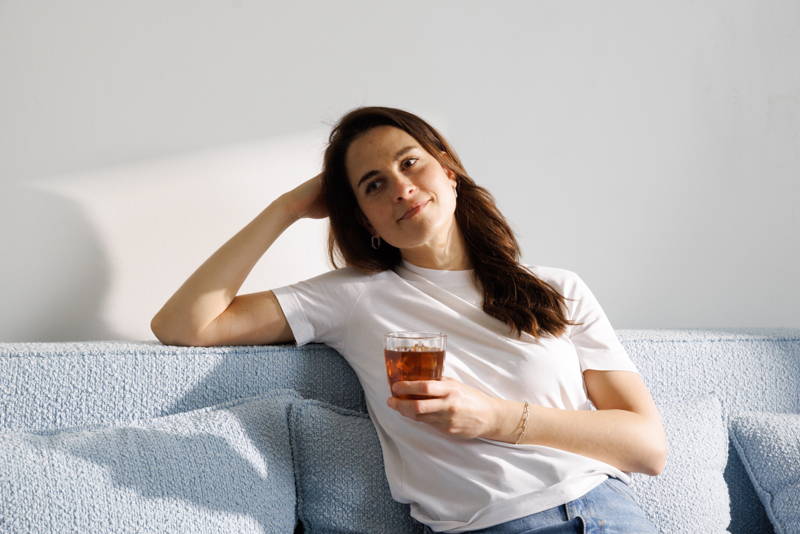 Woman sitting on a sofa, holding a glass of iced coffee