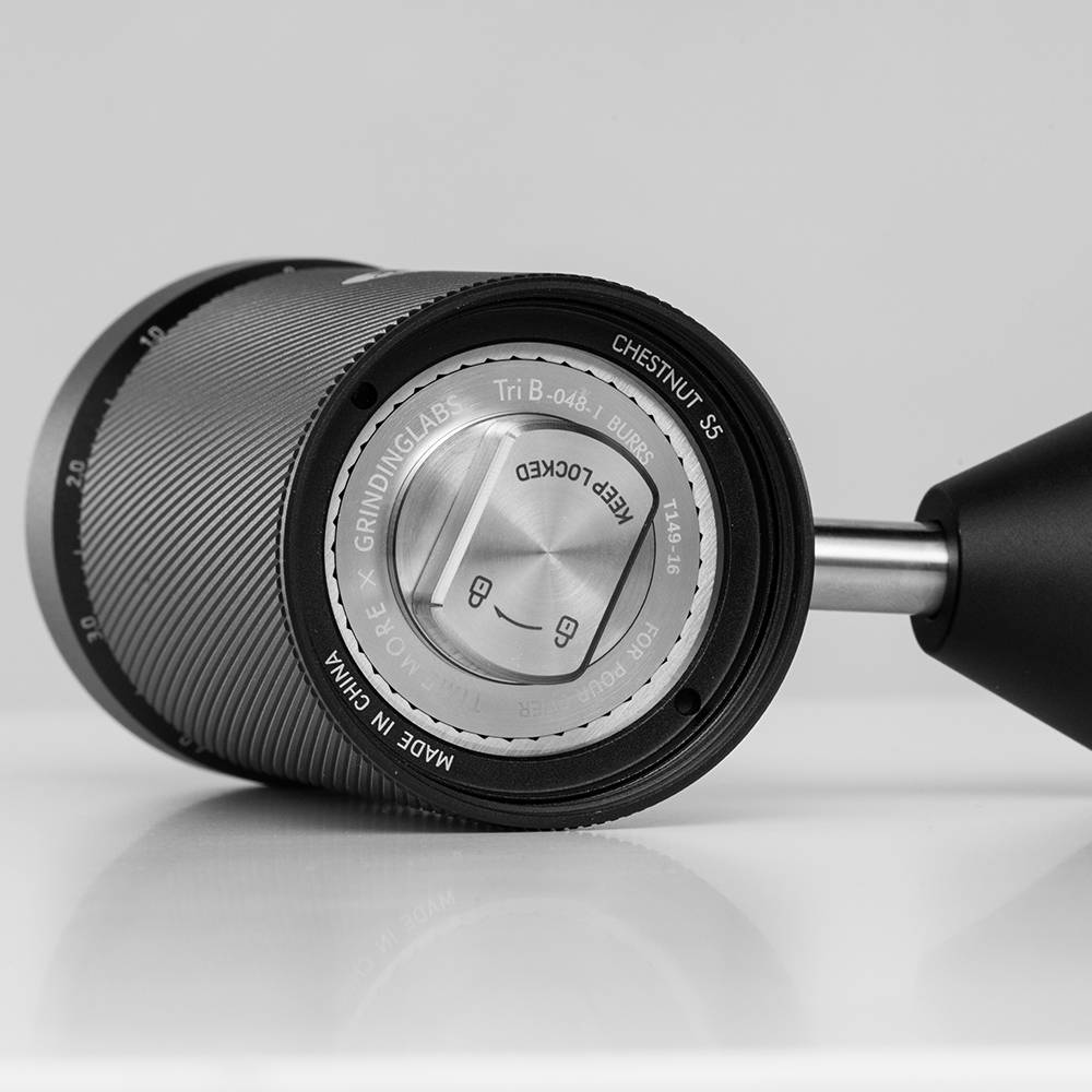  Close-up of the bottom base of the Timemore Chestnut S5 Pro hand grinder, showing the stainless steel burr center, lock indicators, and engravings including "Chestnut S5" and "Tri B-048-1 BURRS".