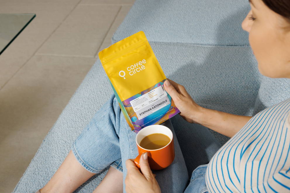 Frau sitzt auf der Couch mit einem Kaffee und einem coffee bag in der Hand