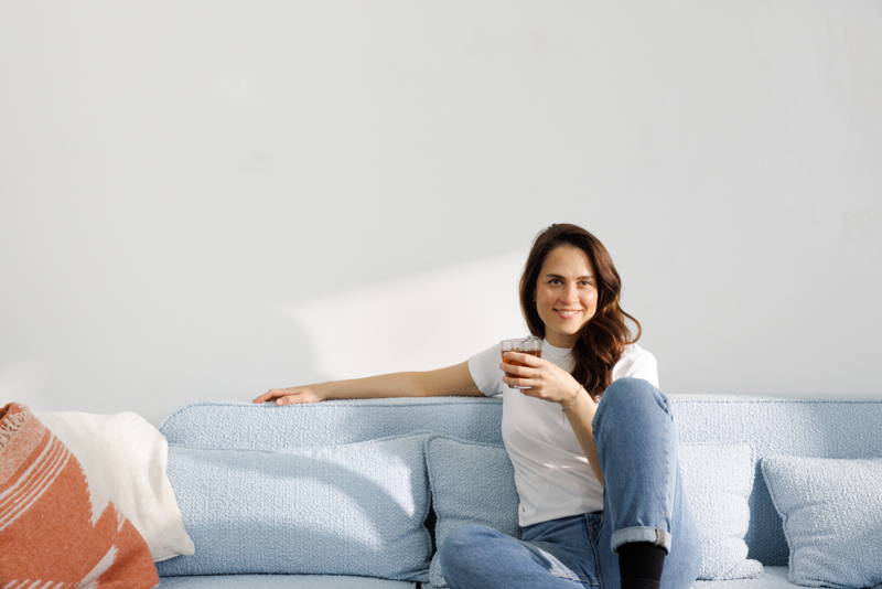 Frau sitzt mit Eiskaffee in der Hand auf der Couch.
