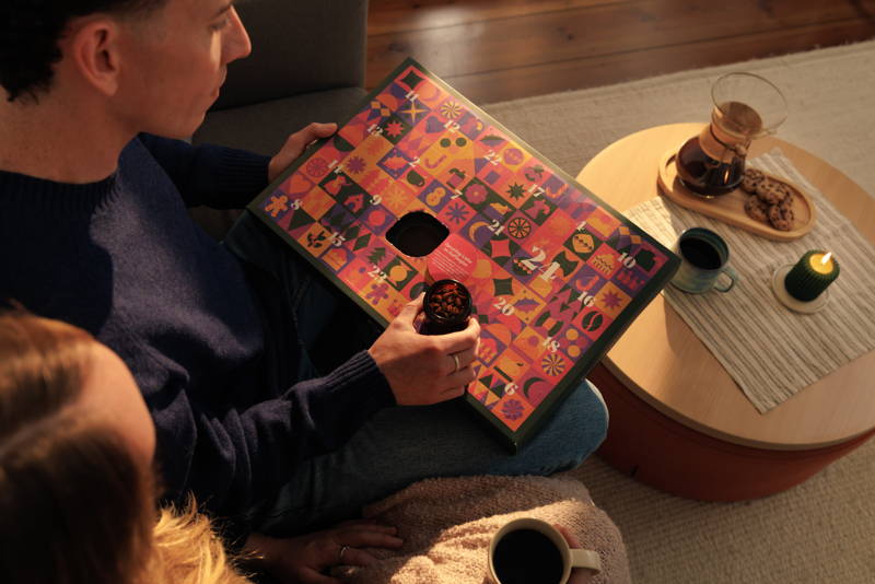 Person öffnet das erste Türchen eines Adventskalenders, auf dem Tisch steht eine Chemex und eine Tasse.