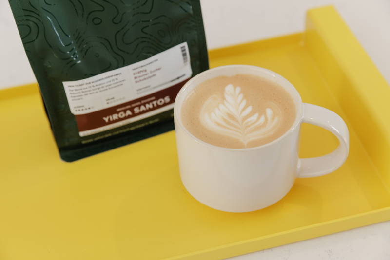 Yirga Santos neben Tasse Kaffee mit Latte Art