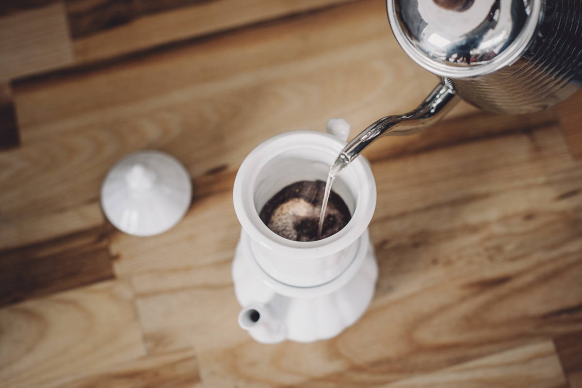 Befeuchte nun zunächst das Kaffeepulver im Porzellanfilter mit einer kleinen Menge Wasser. Warte 30 Sekunden und beobachte, wie der Kaffee zu quellen beginnt. Dieses Aufquellen ist wichtig, denn so kann das Wasser von Anfang an die Aromen besser freigeben. Nach 30 Sekunden gießt du das restliche Wasser vorsichtig in den Wasserverteiler der Kanne (der obere Aufsatz, wie im Bild).