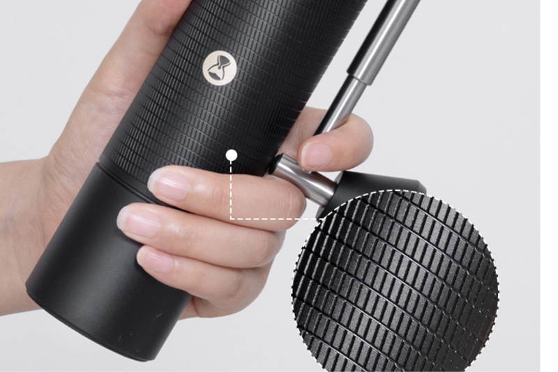 Close-up of a black Timemore manual coffee grinder with a textured surface and a folded metal handle, held by a hand.