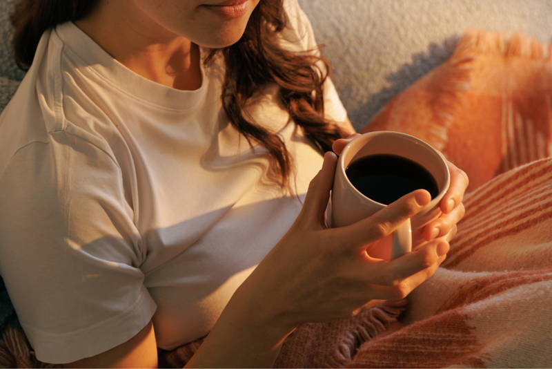Frau sitzt mit Kaffeetasse in der Hand auf der Couch.