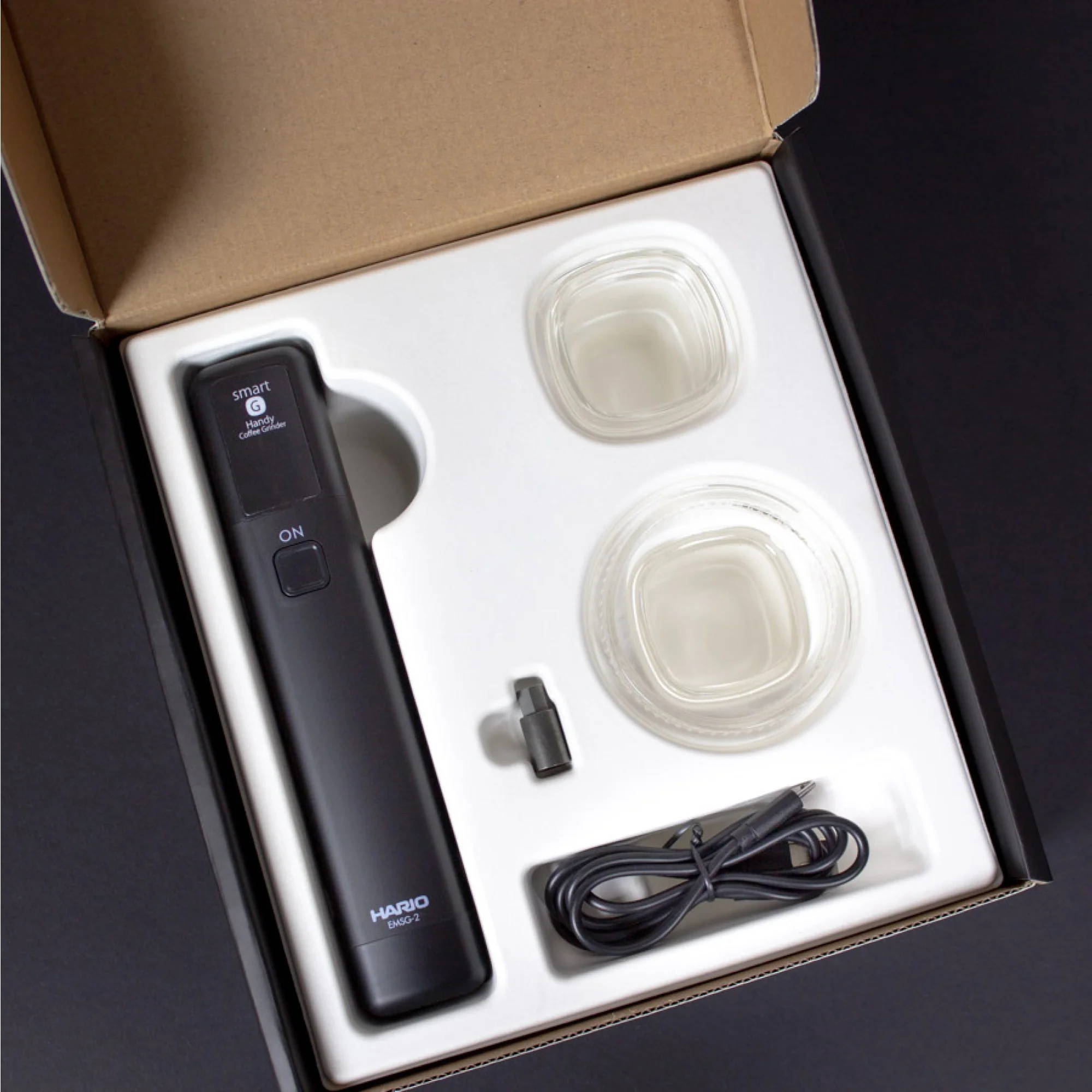The Hario Mobile Stick and Comandante adapter lie on a black background in the packaging.