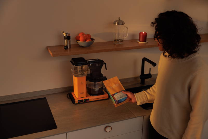 Person hält Hendra Filterkaffee in der Hand und steht vor einem MoccaMaster