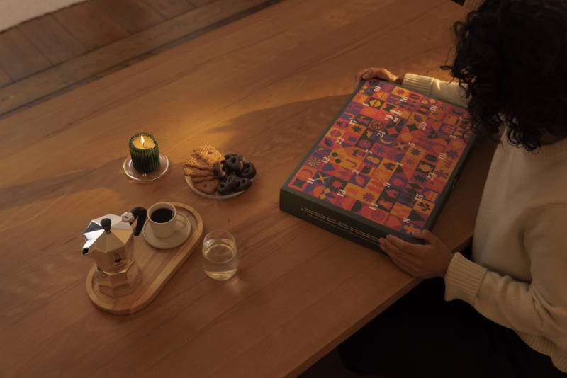 Eine Frau hält einen Adventskalender, auf dem Tisch steht eine Bialetti