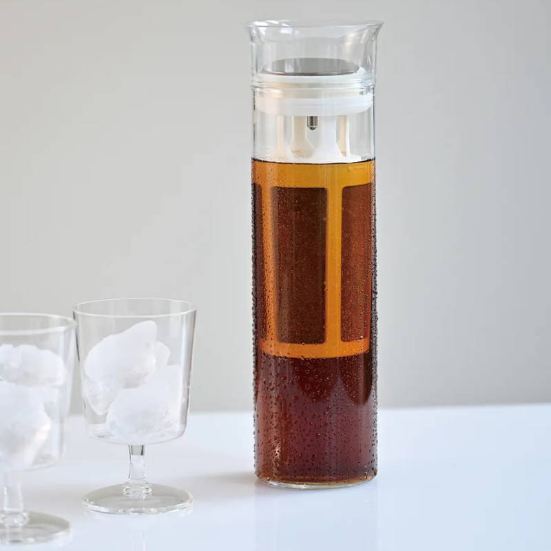Hario Glass Cold Brew Coffee Pitcher stands on a white table. Next to it are two glasses filled with ice cubes.