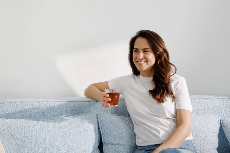 Frau sitzt mit Eiskaffee in der Hand auf der Couch.