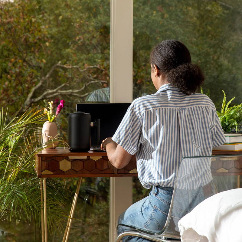 Eine Frau sitzt am Tisch vor ihrem Laptop. Neben ihr steht die Fellow Clara French Press.