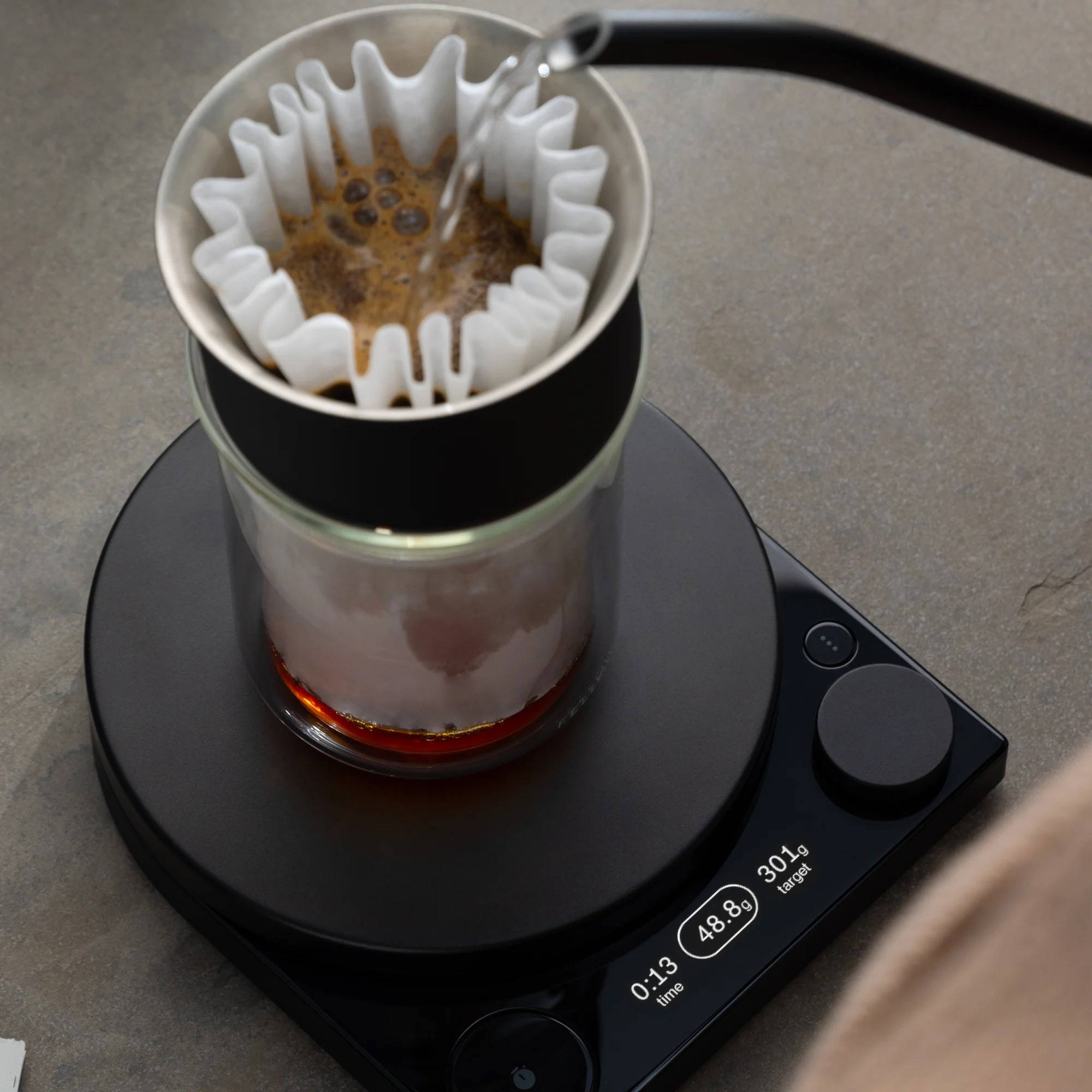 Die Fellow Tally steht auf einem grauen Untergrund. Auf der Tally befindet sich der Fellow Stagg X Pour Over Dripper und wir mit Wasser befüllt.