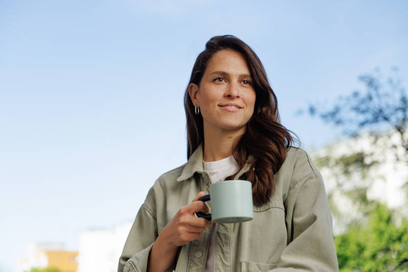 Frau steht auf Balkon und hält Kaffeetasse in der Hand