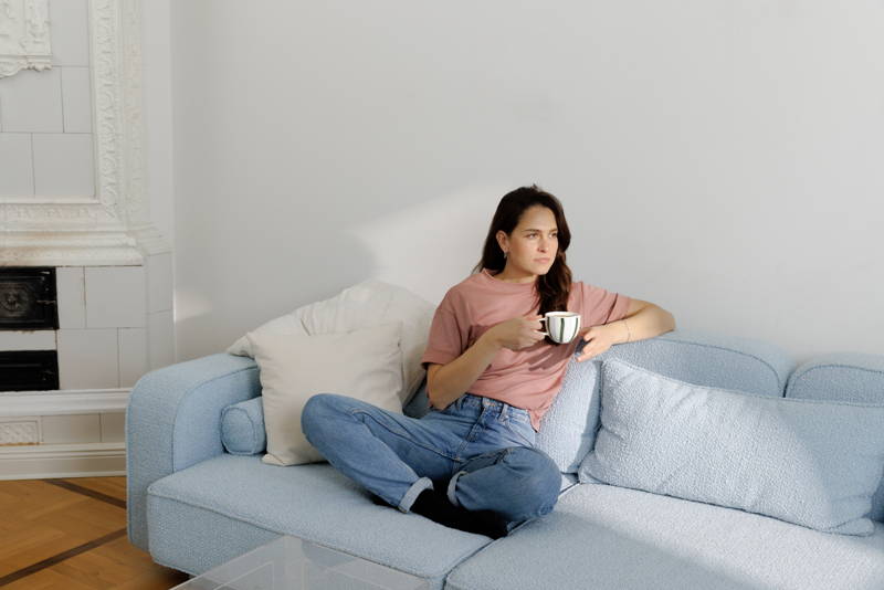 Frau sitzt mit Kaffeetasse in der Hand auf der Couch.