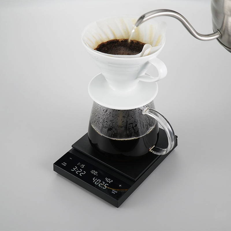 The Hario Polaris coffee scale is shown on a gray background. On the scale are a pot and a Hario V60 hand filter.