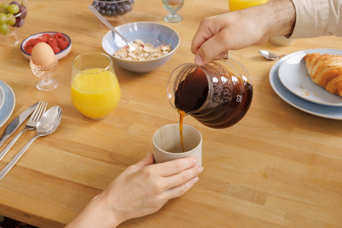 Frühstückstisch, Kaffee wird aus einer Kanne in eine Tasse eingeschenkt.