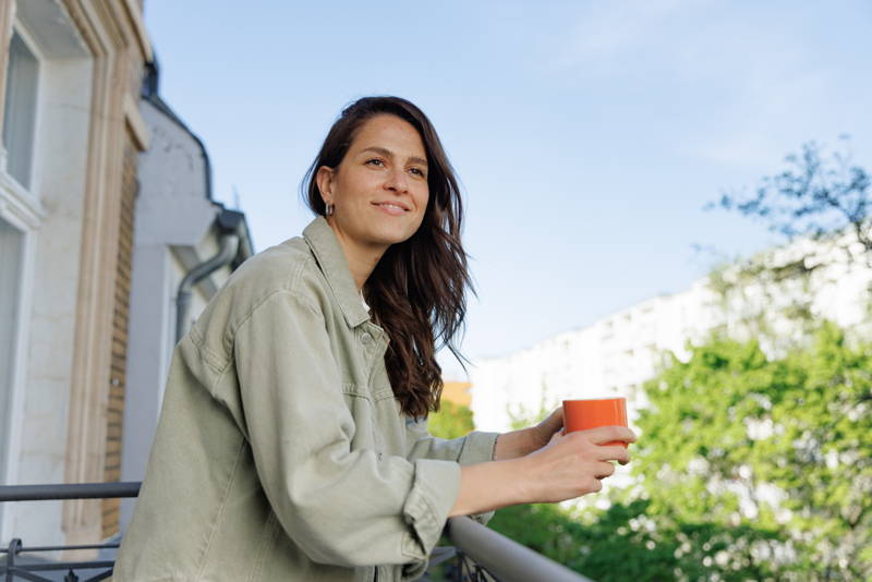 Woman standing on balcony holding coffee cup in her hand