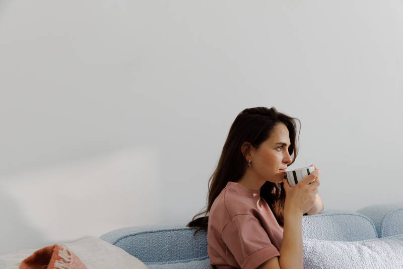 Frau sitzt mit Kaffeetasse in der Hand auf der Couch.