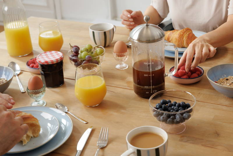 A man and a woman are sitting at the breakfast table drinking coffee from a French press.