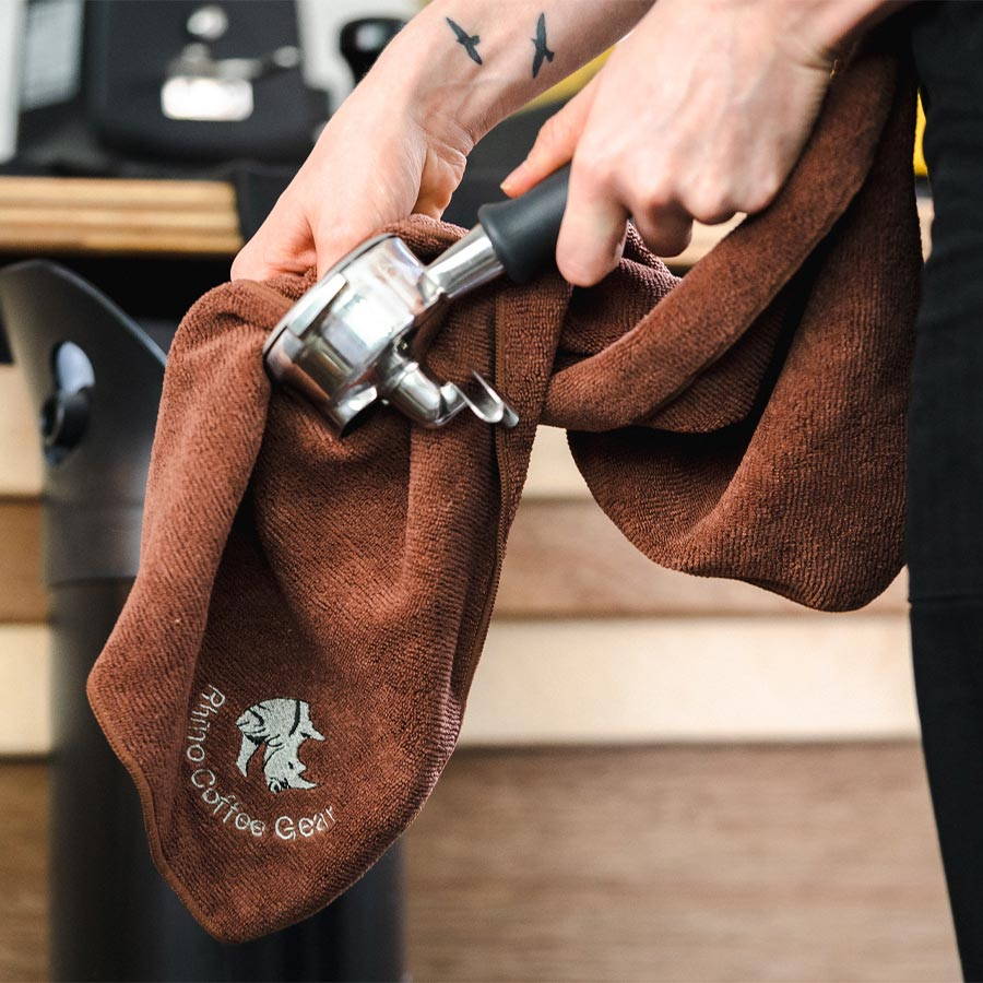 A man cleans a portafilter with the brown Rhinware barista cloth.