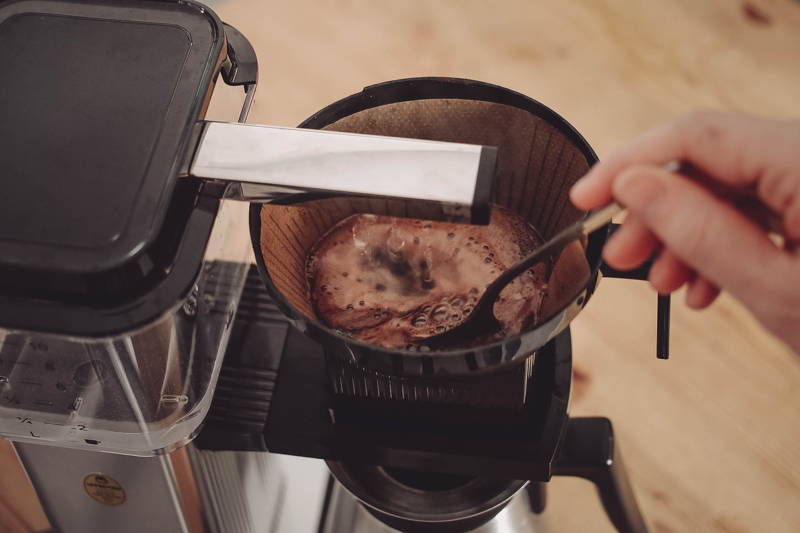 Um sicher zu stellen, dass das Kaffeemehl vollständig mit Wasser bedeckt ist, rühre es noch einmal unter das Wasser.