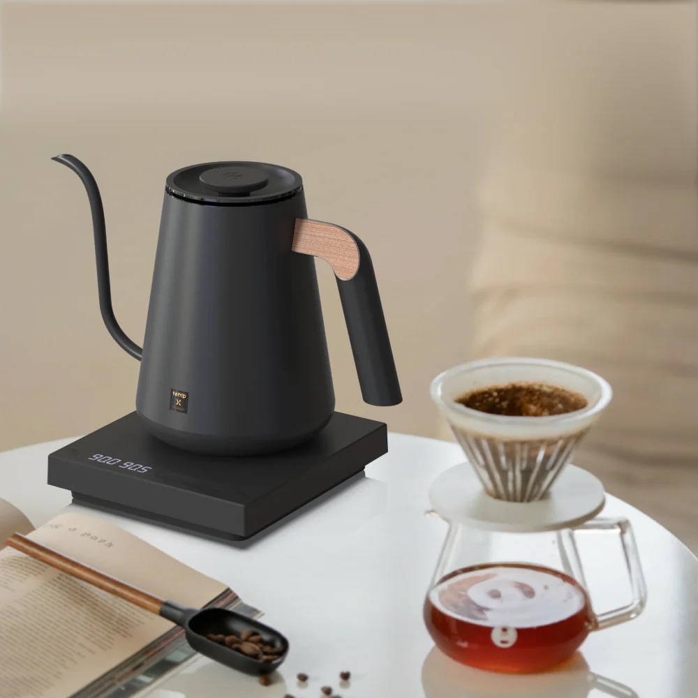 Mattbraun-schwarzer elektrischer Schwanenhals-Wasserkocher mit Holzgriff auf einer digitalen Basis, daneben ein Kaffeefilter auf einer Glaskanne.