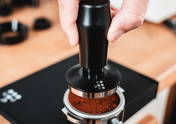 Eine Hand hält einen schwarzen Coyooco Tamper, um Kaffeepulver im Siebträgern zu tampen.