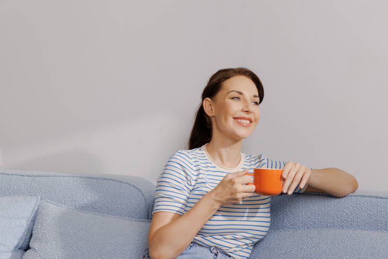 Frau sitzt auf der Couch mit einem Kaffee in der Hand