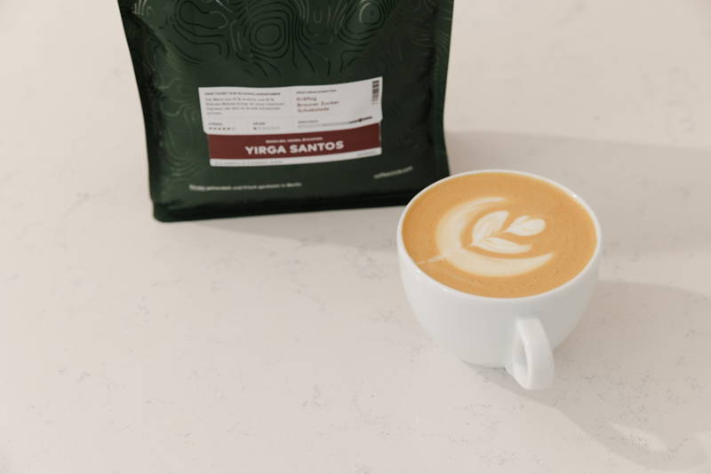 Yirga Santos neben Tasse Kaffee mit Latte Art
